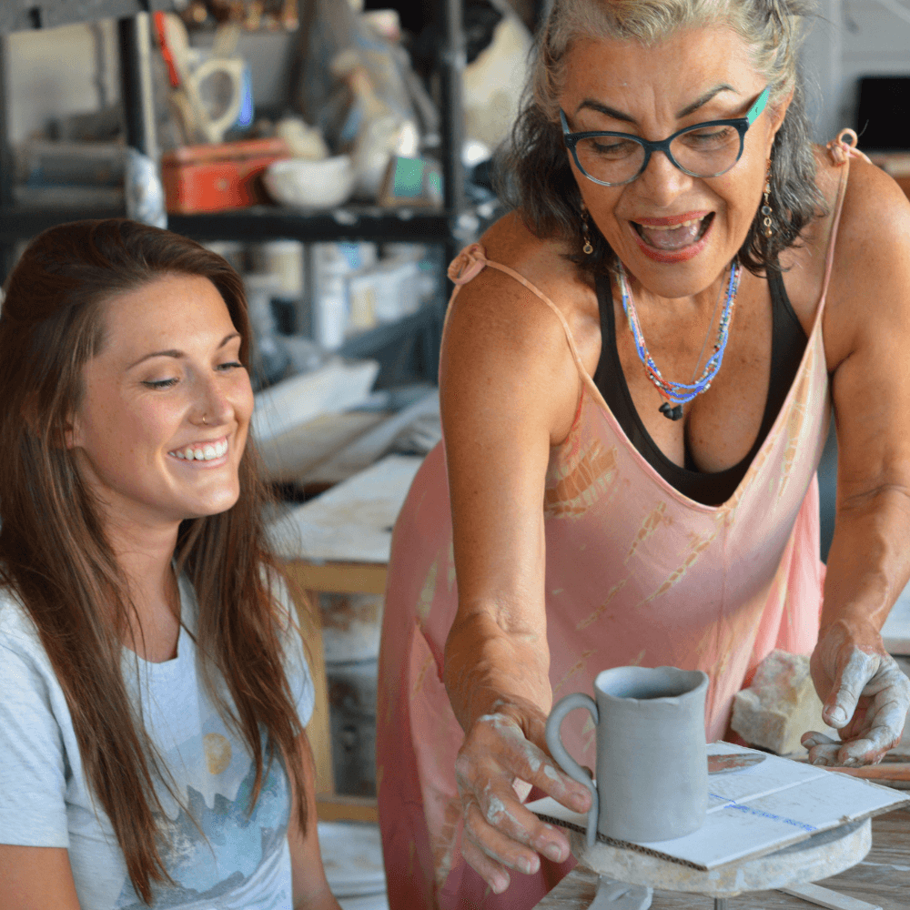 The experienced María Esther Galbán, a woman clay artist from Venezuela, teaching a young female how to craft a ancient clay mug.
